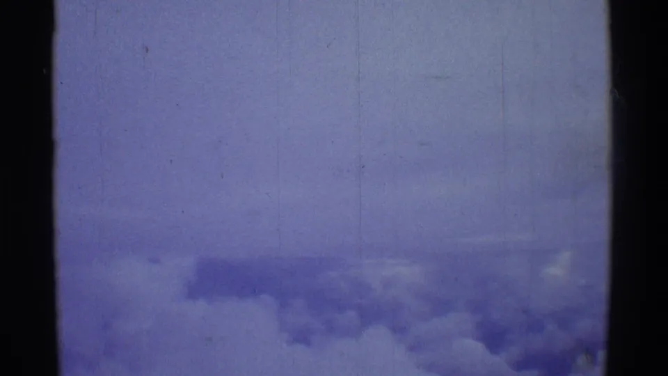 Final 8mm travel frame showing a pale aerial cloud view over Hawaii with scratches, dust, and blue color drift.