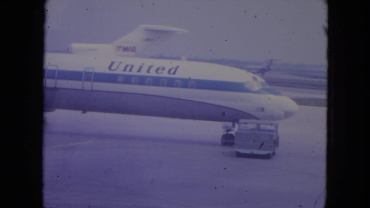 1972 O'Hare frame with United lettering on an aircraft fuselage and a ramp vehicle positioned near the nose gear.