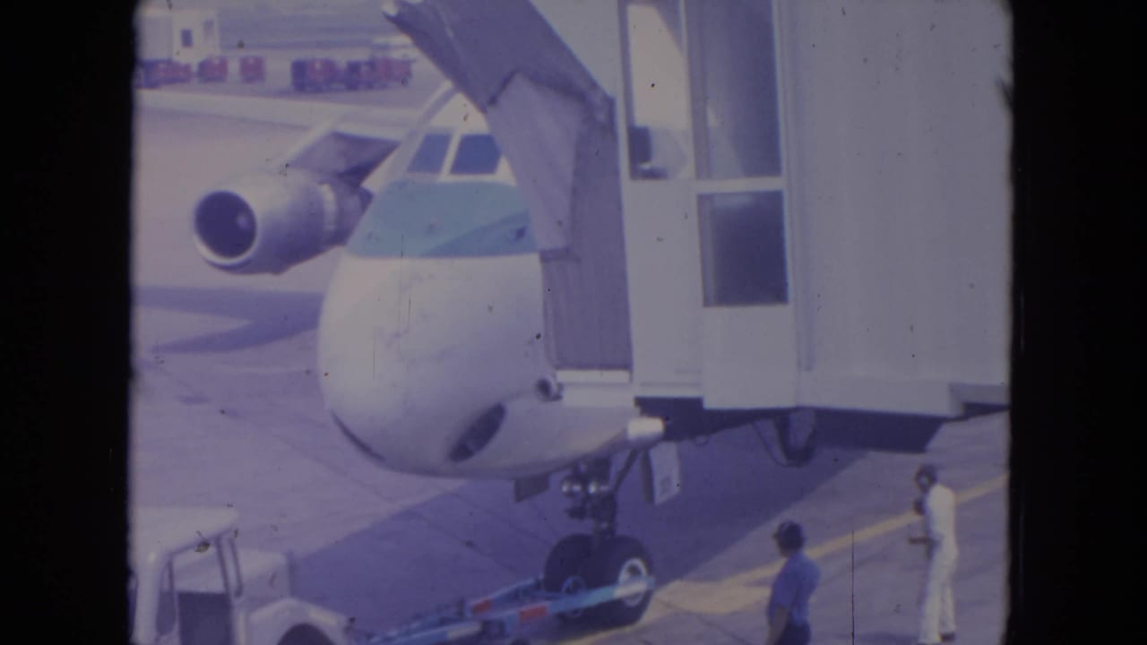 Commercial jet nose at a gate with jet bridge and ground crew on the tarmac.