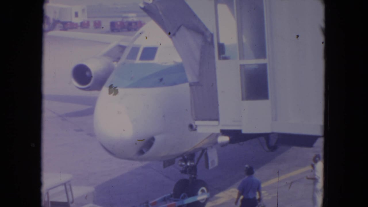 1972 O'Hare frame of a commercial airliner at the gate, with its cockpit, engine intake, and ramp workers visible.