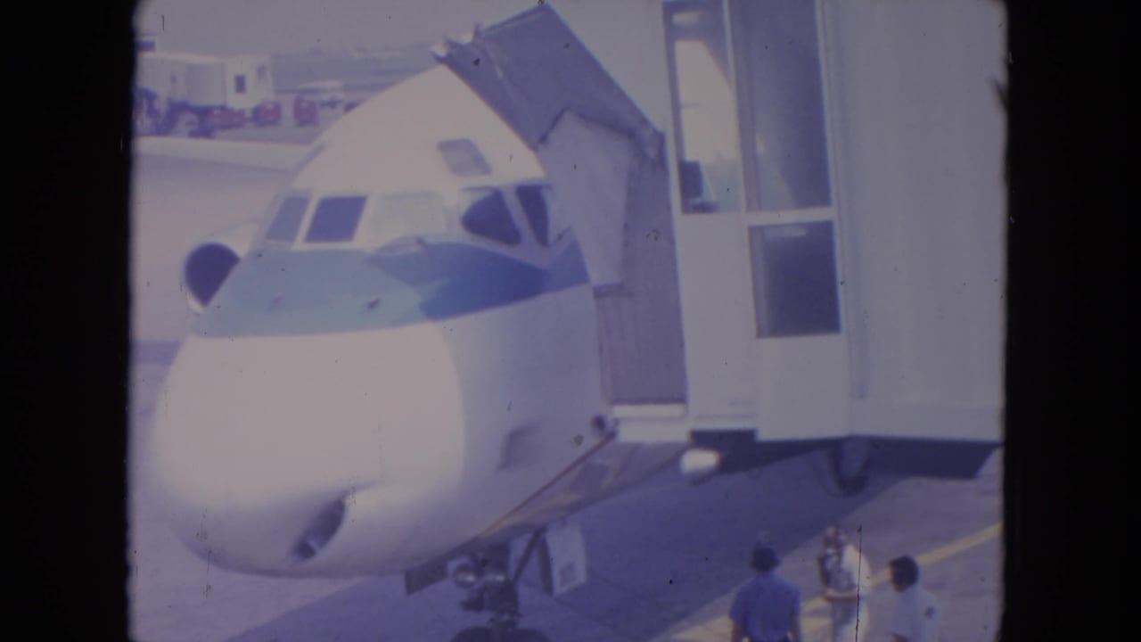1972 O'Hare 8mm frame showing a parked commercial jet at a gate, with ground crew and jet bridge details visible.