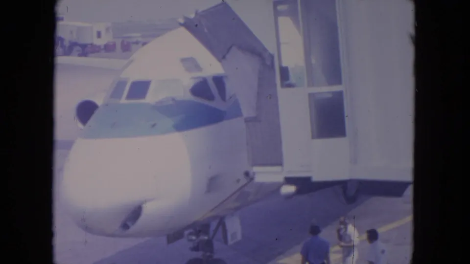 1972 O'Hare 8mm frame showing a parked commercial jet at a gate, with ground crew and jet bridge details visible.