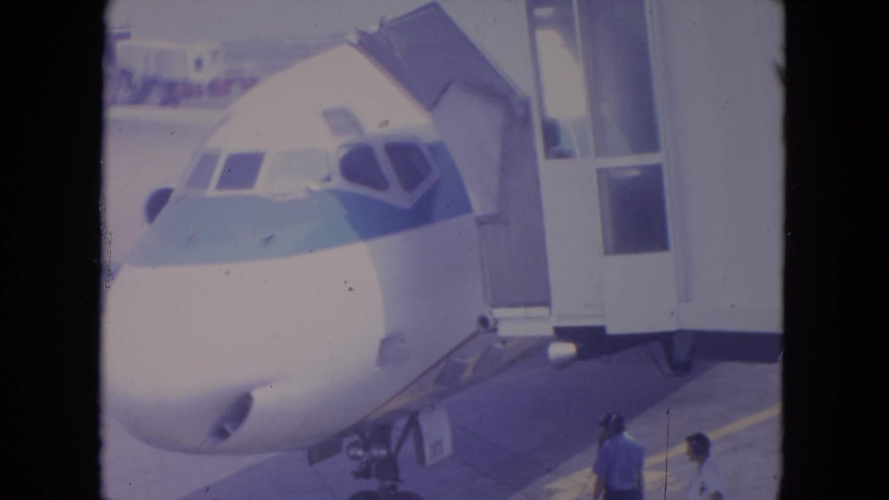 Commercial airliner nose at a gate with people standing below near boarding equipment.