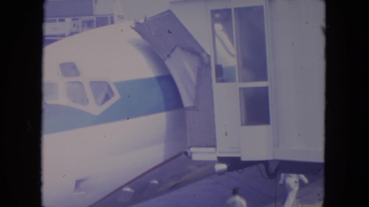 O'Hare home-movie frame showing the aircraft nose, boarding access structure, and people moving near the bottom of the tarmac view.