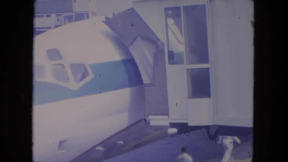 O'Hare home-movie frame showing the aircraft nose, boarding access structure, and people moving near the bottom of the tarmac view.