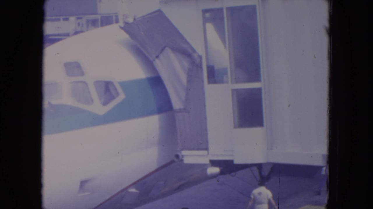 Airliner nose beside a jet bridge at an airport gate, with terminal windows in the background.