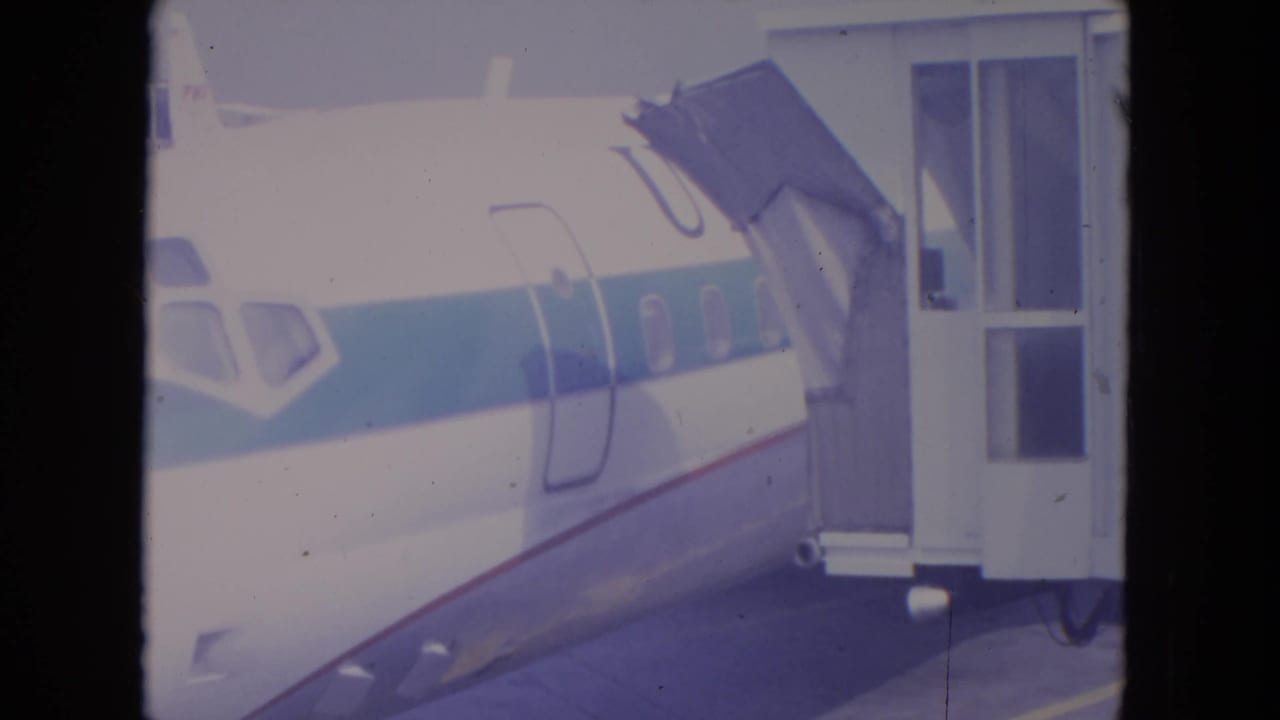 White commercial airplane beside a jet bridge at an airport gate.