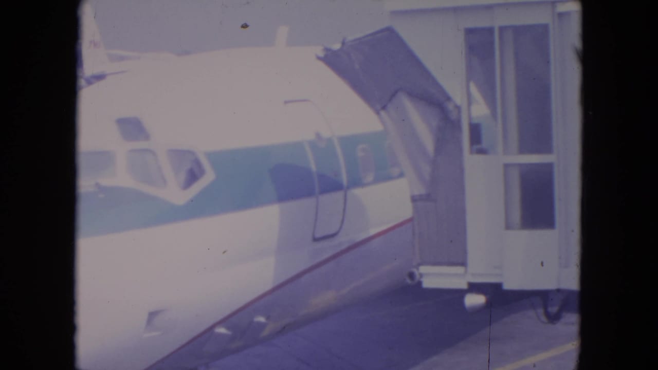 1972 O'Hare airport frame showing a commercial airplane beside a terminal jet bridge, scanned from 8mm home-movie film.