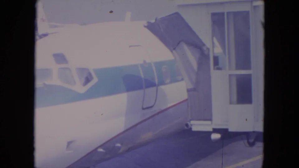1972 O'Hare airport frame showing a commercial airplane beside a terminal jet bridge, scanned from 8mm home-movie film.