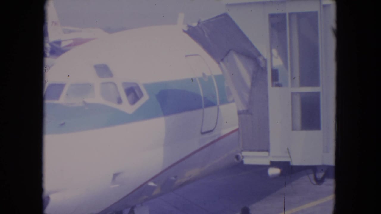 1972 O'Hare 8mm frame showing the jet cockpit area, striped fuselage, and connected passenger bridge.