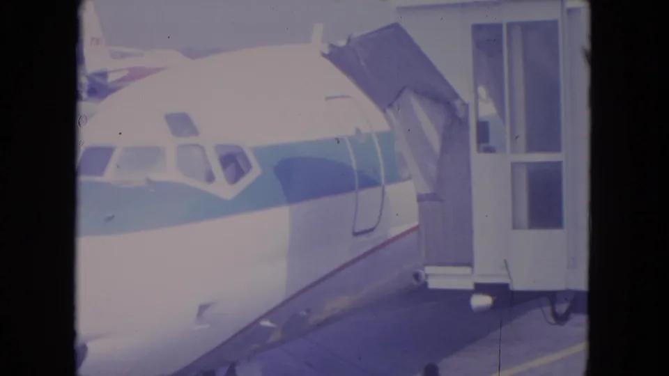 1972 O'Hare 8mm frame showing the jet cockpit area, striped fuselage, and connected passenger bridge.