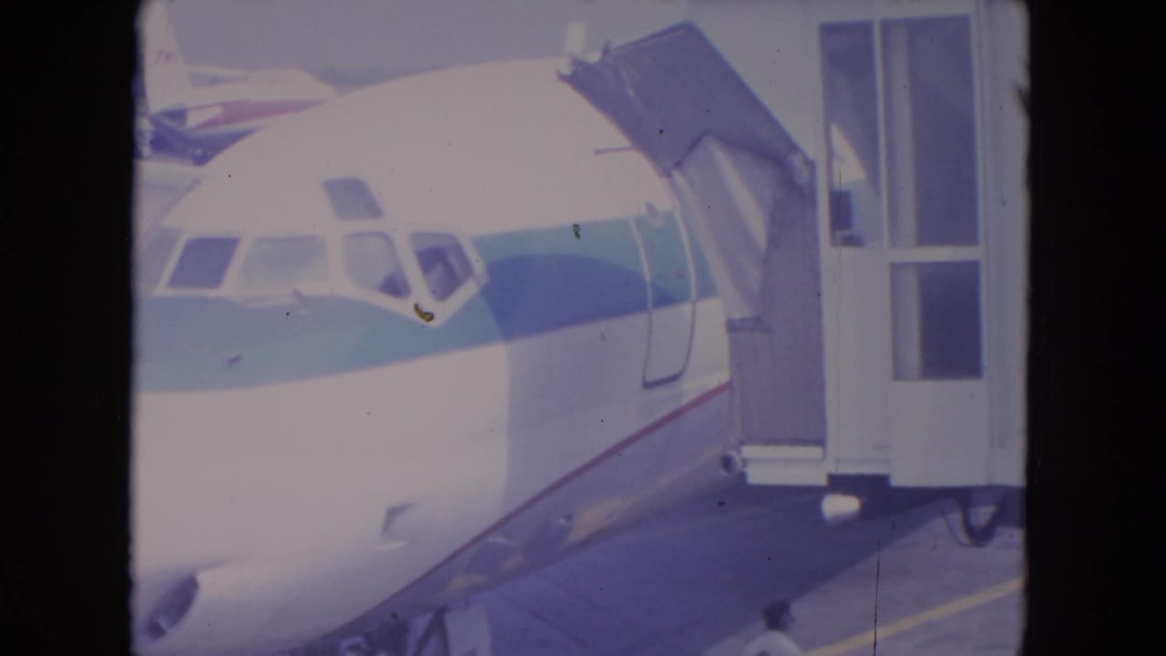 1972 O'Hare frame showing a parked commercial jet with the boarding bridge extended under bright daylight.