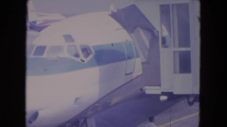 1972 O'Hare frame showing a parked commercial jet with the boarding bridge extended under bright daylight.