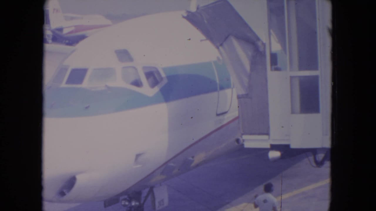 Jet nose parked at a gate with a jetway connected and tarmac below.
