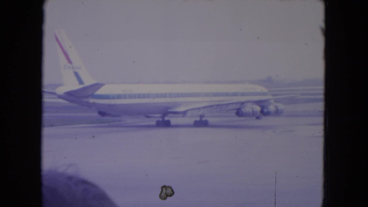 1972 O'Hare frame of a commercial jet moving along the tarmac in side view, with visible film dust and faded color from the 8mm source.