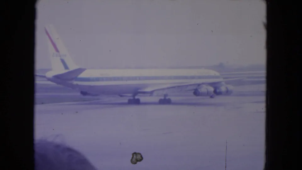 1972 O'Hare frame of a commercial jet moving along the tarmac in side view, with visible film dust and faded color from the 8mm source.
