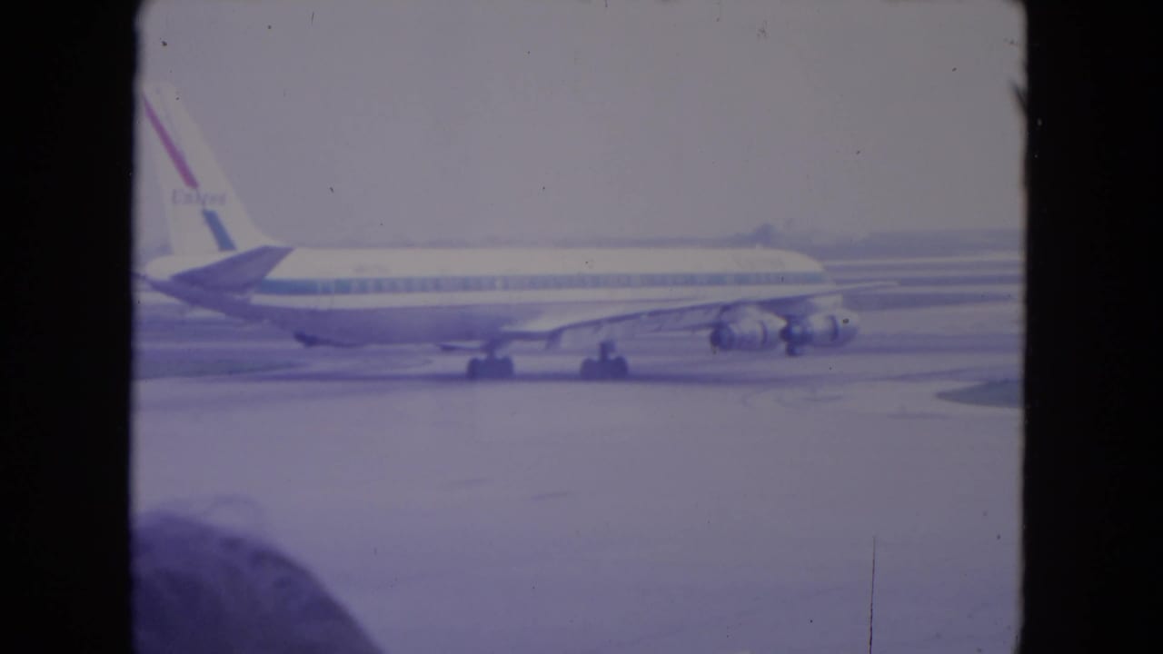 A United Airlines jet appears on the O'Hare tarmac in 1972 home-movie footage, framed by a dark terminal-window edge.