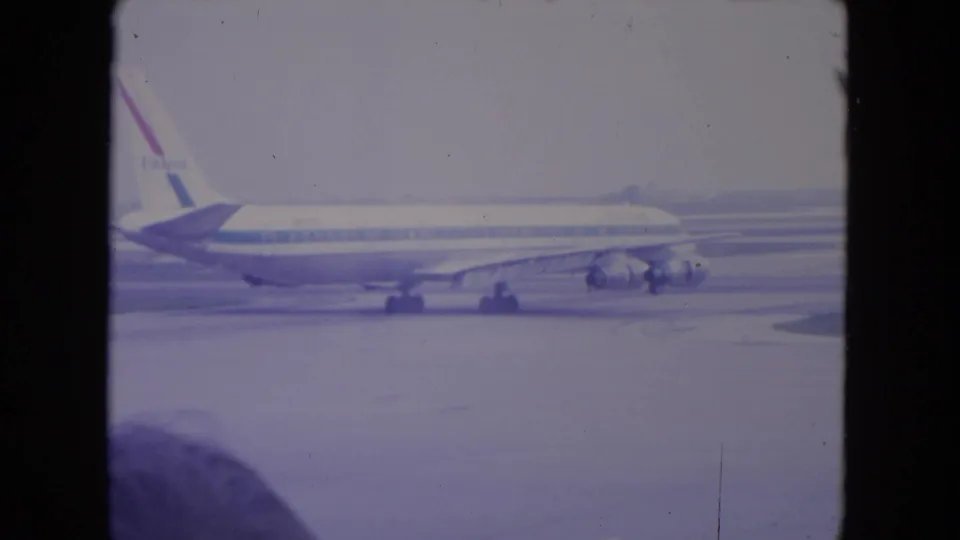 A United Airlines jet appears on the O'Hare tarmac in 1972 home-movie footage, framed by a dark terminal-window edge.
