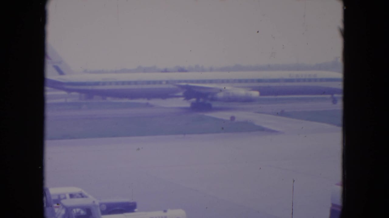 The United jet remains in view on the O'Hare tarmac while a car appears near the bottom edge of the 8mm frame.
