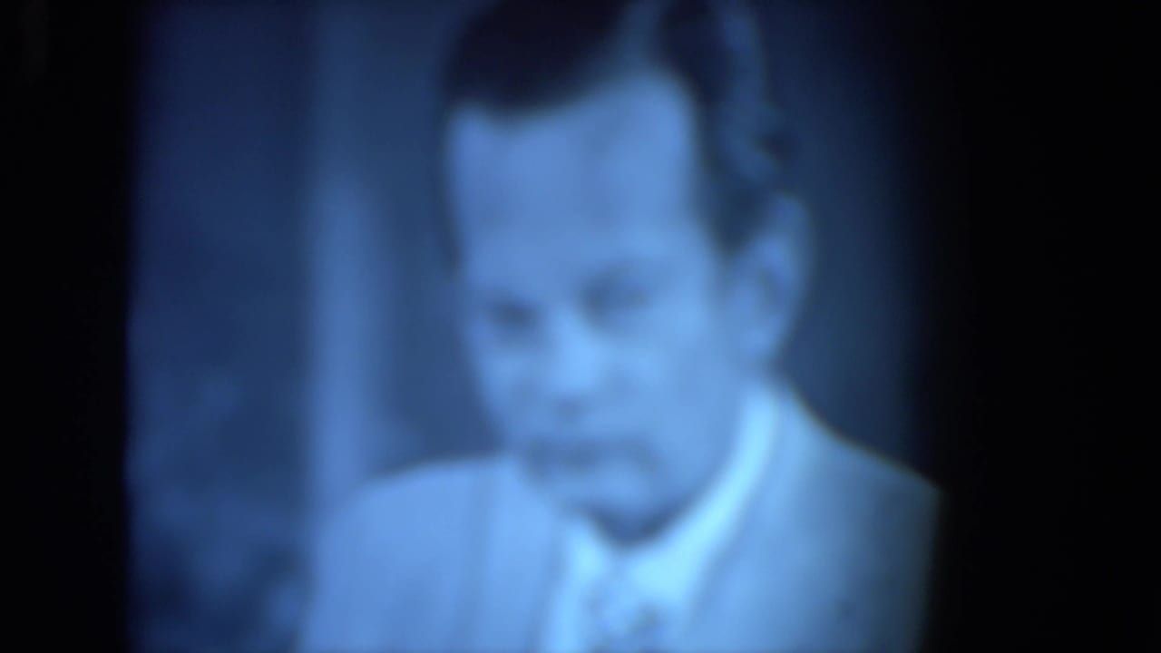 Blurry 1972 O'Hare Chicago 8mm view of a suited man with a tie, seen close-up through a blue-tinted flickering image.