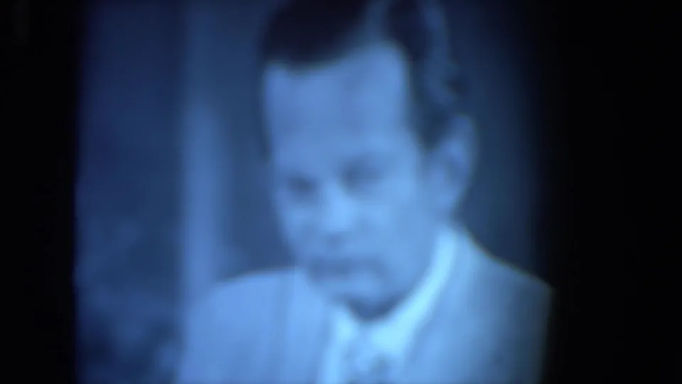 Blurry 1972 O'Hare Chicago 8mm view of a suited man with a tie, seen close-up through a blue-tinted flickering image.