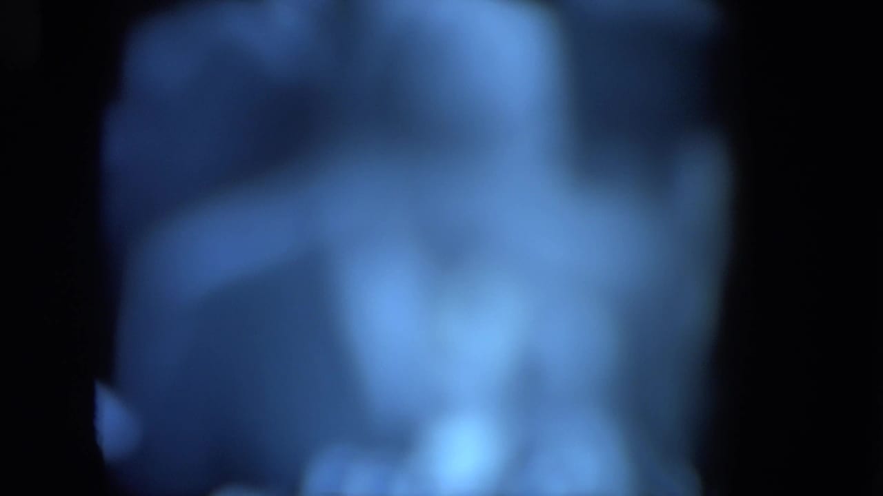 Very blurred blue-tinted frame with indistinct figures and dark film borders.