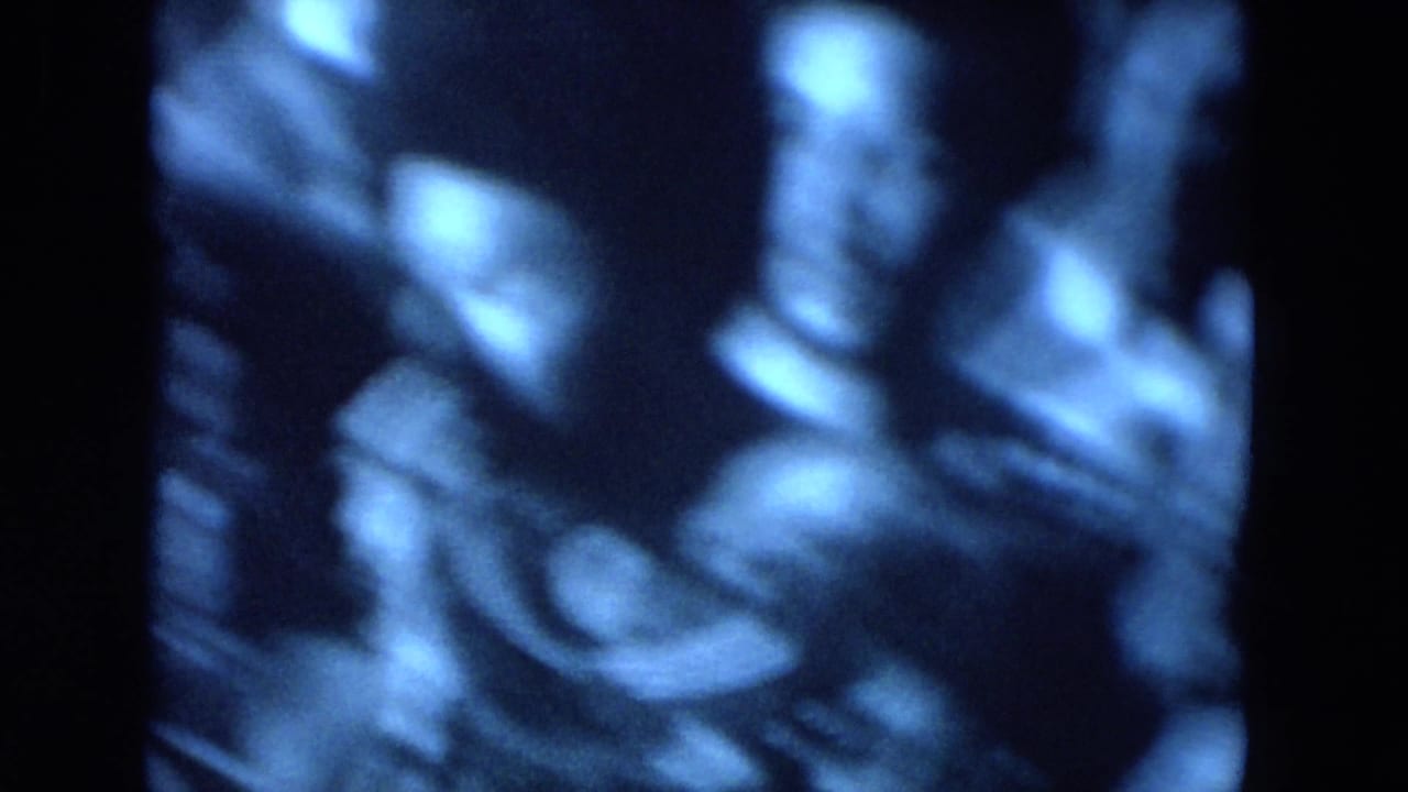 Blue-tinted crowd scene with several people seated or gathered close together.