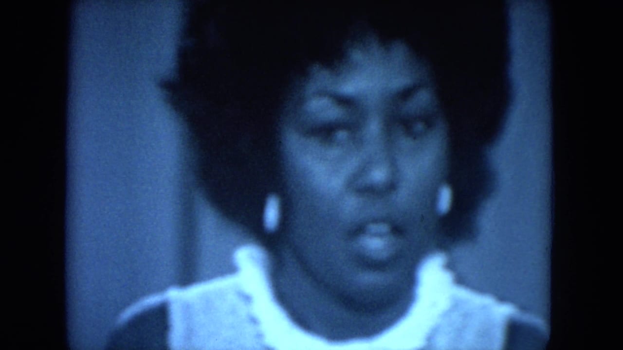 Close-up of the Black woman speaking at the 1972 O'Hare Chicago gathering, with white collar, earrings, and blue 8mm grain visible.