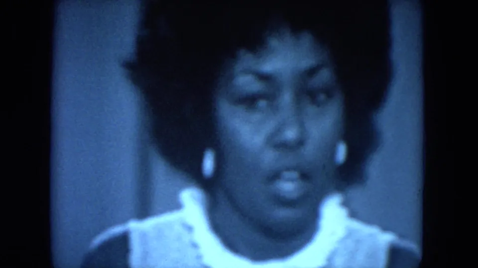 Close-up of the Black woman speaking at the 1972 O'Hare Chicago gathering, with white collar, earrings, and blue 8mm grain visible.