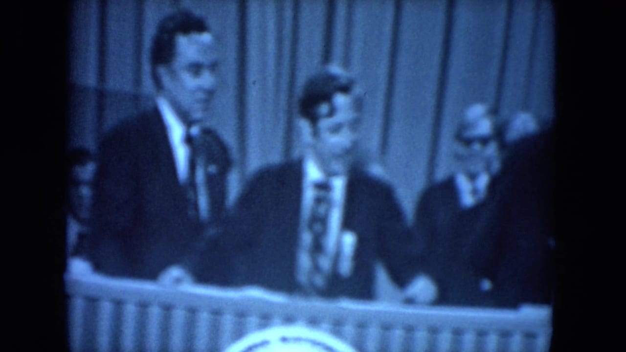 Several suited men stand behind microphones at a formal dais.