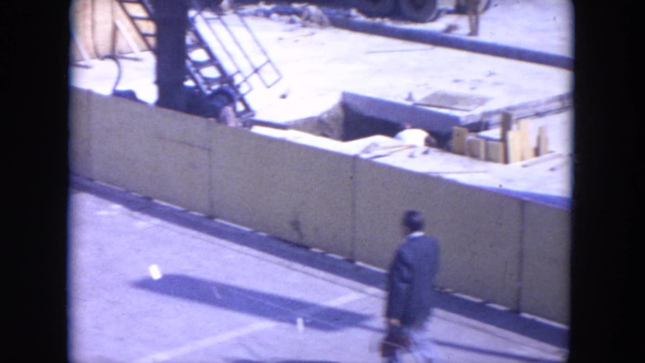 1972 O'Hare Chicago 8mm frame showing a suited man with briefcase near fencing, excavation, and scaffolding.