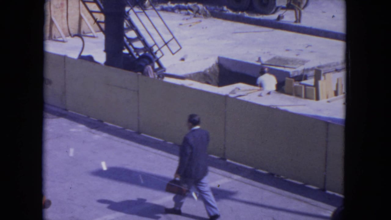 Man in a dark jacket carries a briefcase past a construction barrier.
