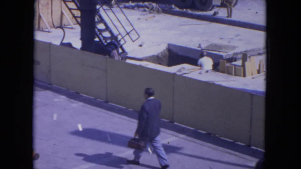 At O'Hare Chicago in 1972, a suited man with a briefcase walks along pavement beside a construction barrier.