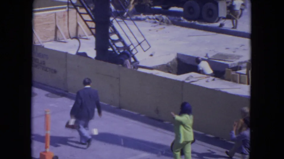 At O'Hare Chicago in 1972, pedestrians move past a construction barrier while a woman in a bright green suit approaches.