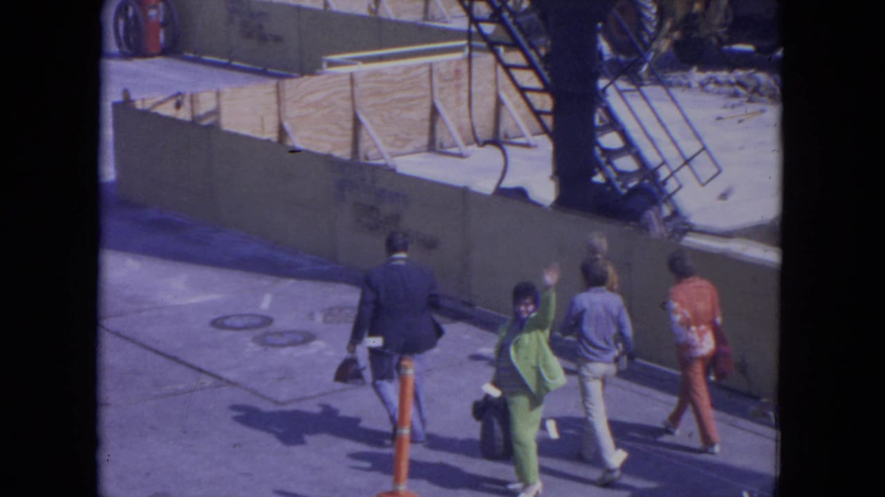 At O'Hare Chicago in 1972, a small group walks along the street while a woman in green and others wave toward the camera.