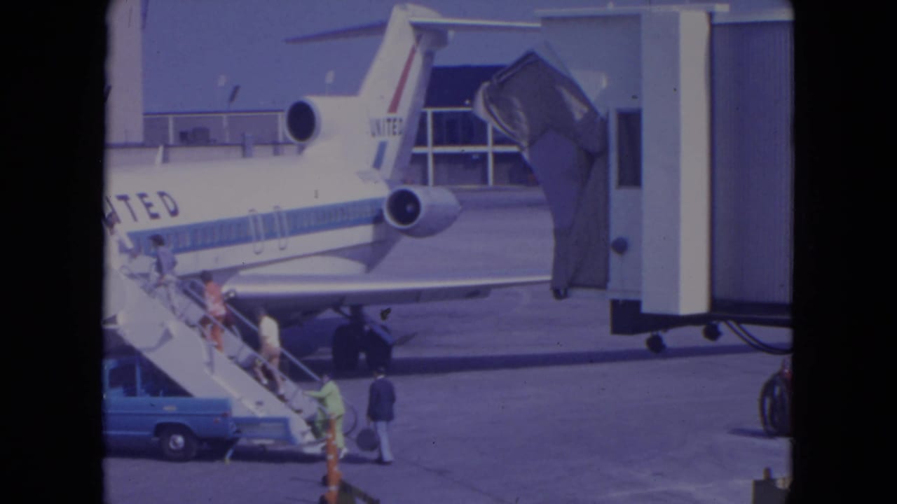 At the airport apron, passengers board a United jet by mobile stairs while a blue service vehicle sits nearby.