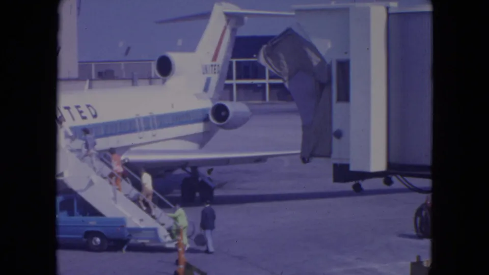 At the airport apron, passengers board a United jet by mobile stairs while a blue service vehicle sits nearby.