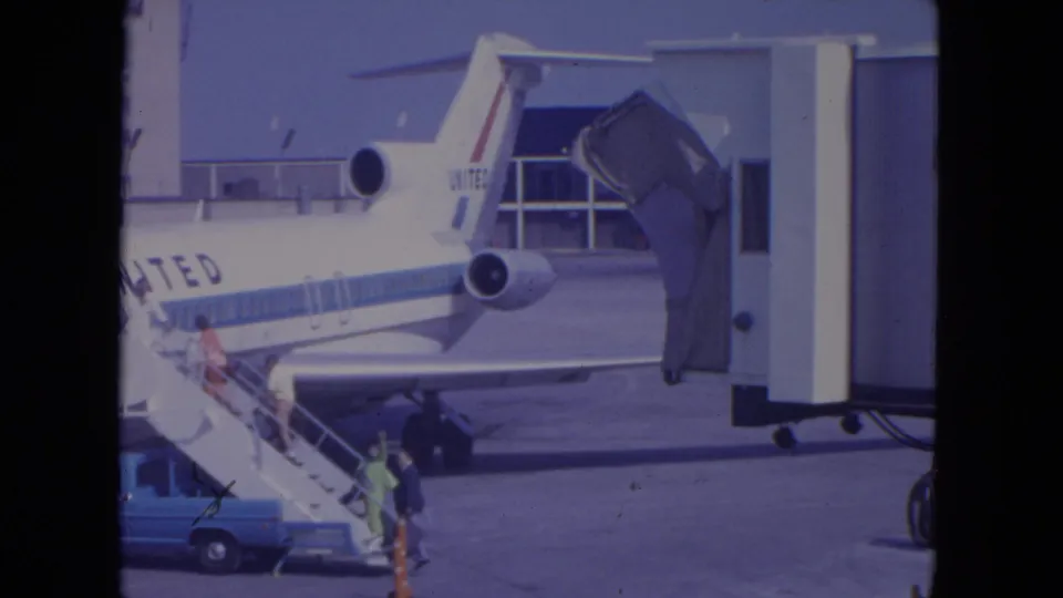 At O'Hare in 1972, a United jet remains parked near a jet bridge while passengers continue boarding by mobile stairs.