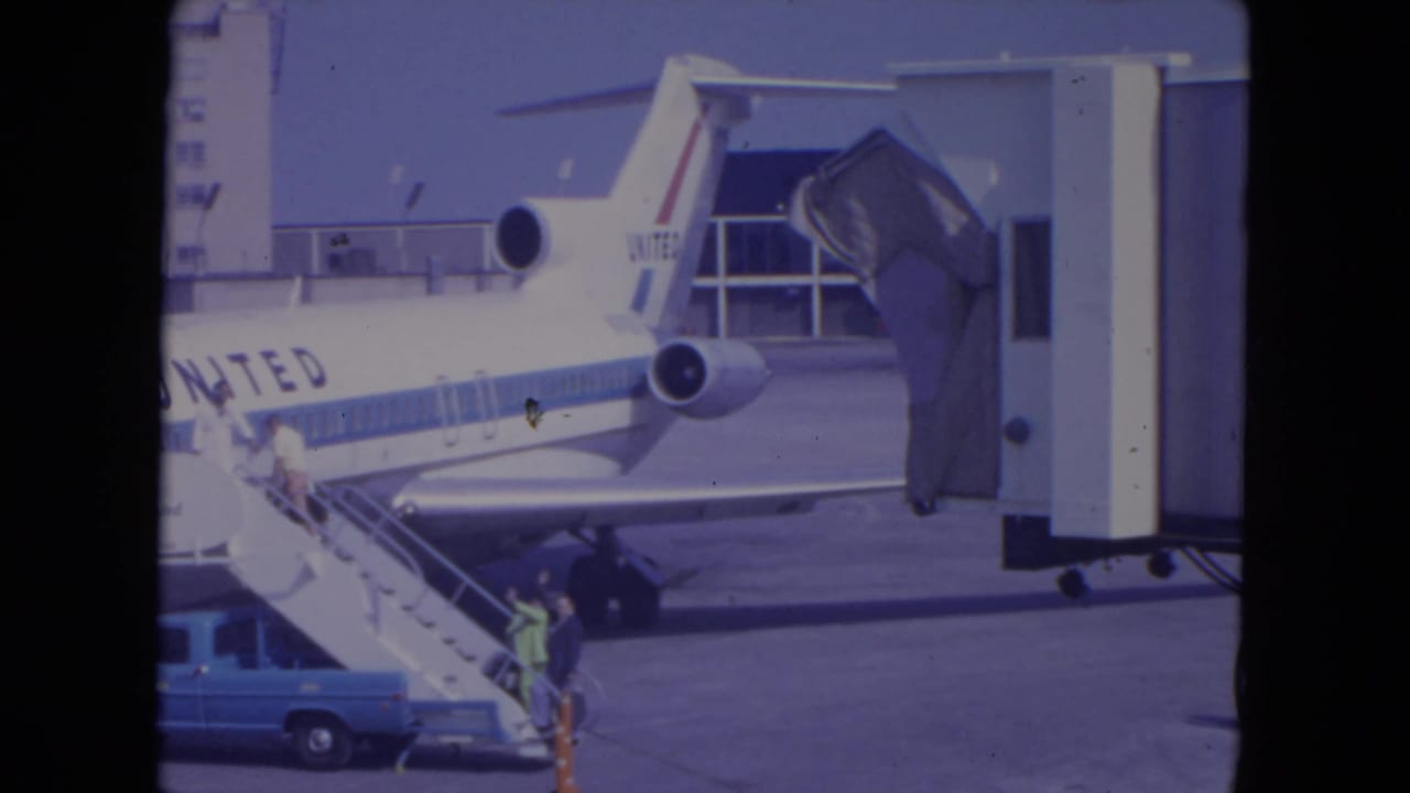 United Airlines aircraft at a gate with passengers on stairs and a blue truck below.