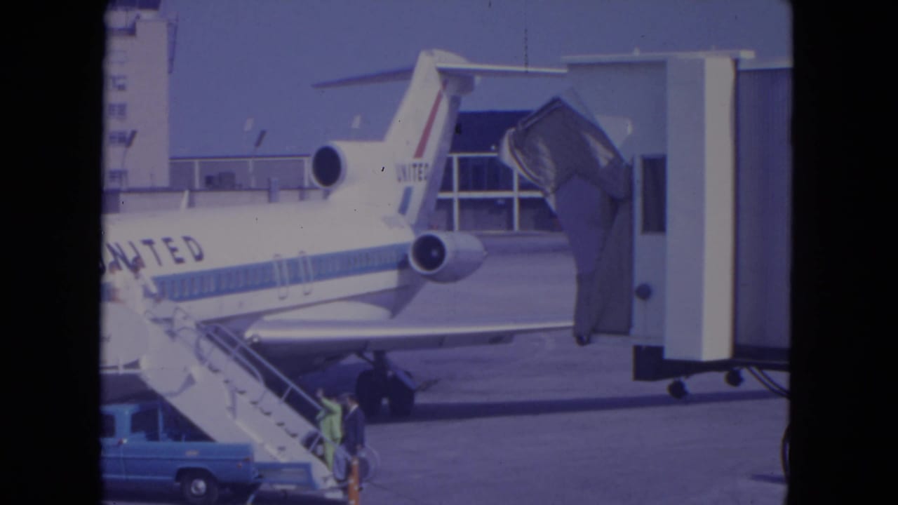 1972 O'Hare home-movie frame of a passenger climbing mobile stairs beside a United Airlines jet connected near a gate area.