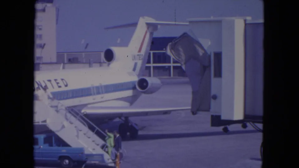 1972 O'Hare home-movie frame of a passenger climbing mobile stairs beside a United Airlines jet connected near a gate area.