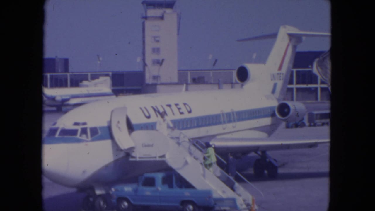 1972 O'Hare frame showing the nose and fuselage of a United Airlines jet with exterior boarding stairs and ground vehicle nearby.