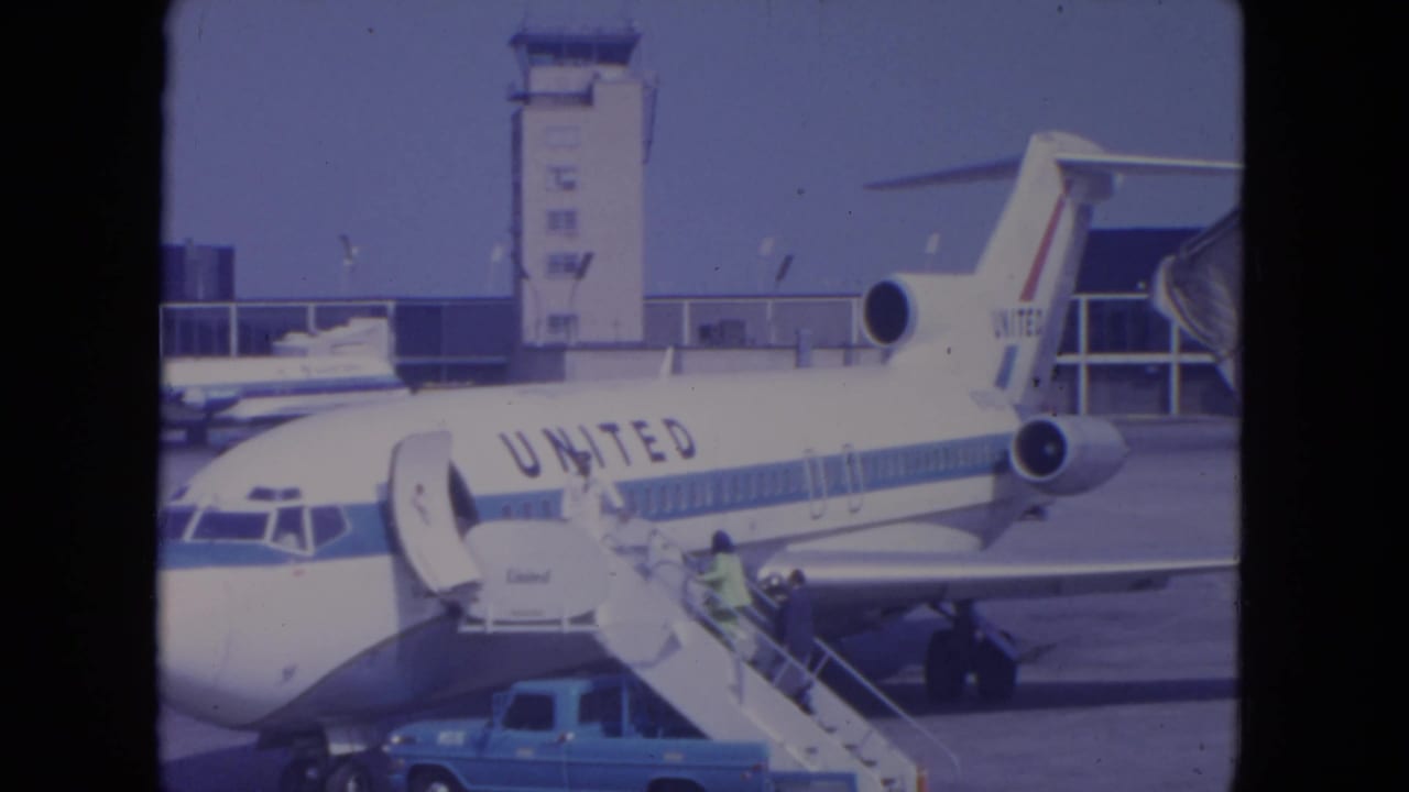 United Airlines jet at a gate with mobile stairs and ramp activity nearby.