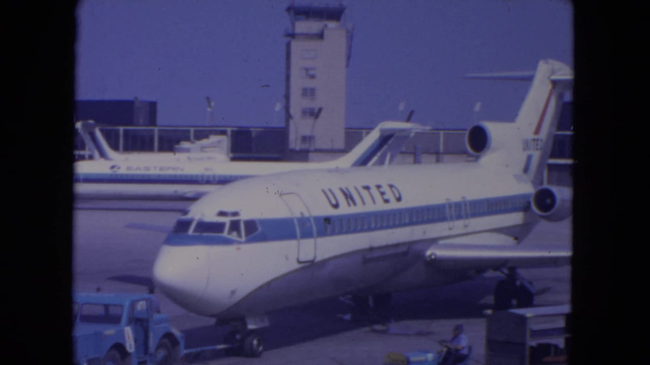 Wide 1972 O'Hare view of a United Airlines jet on the apron with control tower, another aircraft, and ground vehicles visible.