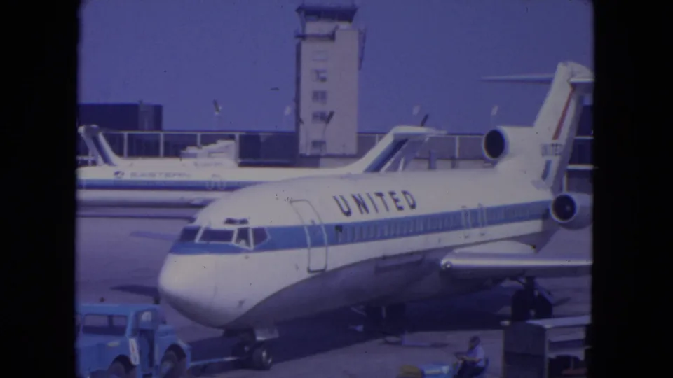 Wide 1972 O'Hare view of a United Airlines jet on the apron with control tower, another aircraft, and ground vehicles visible.