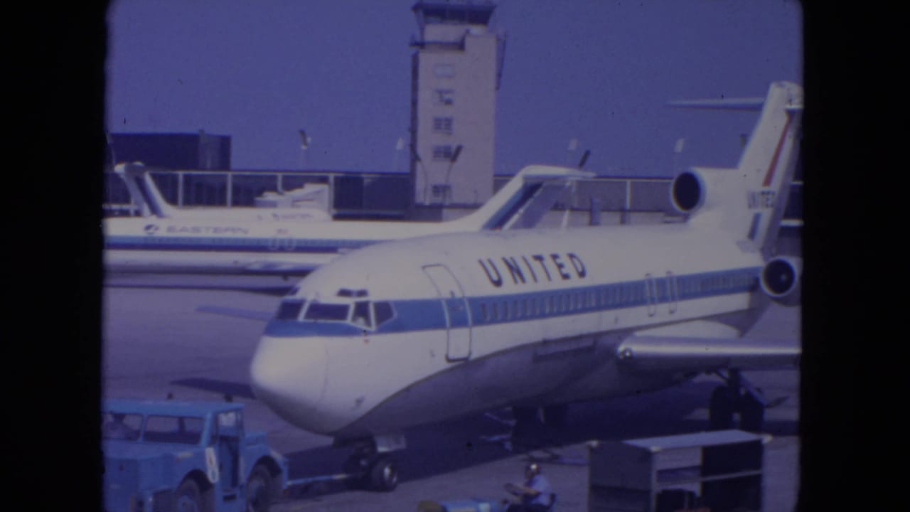 United jet parked on an airport tarmac with a control tower and another aircraft behind it.