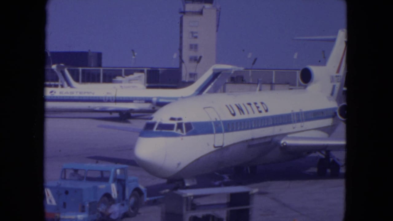 Front section of a United jet on the tarmac with service vehicles and airport structures nearby.
