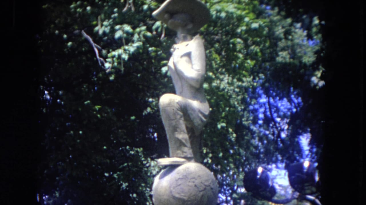 Stone garden sculpture partly framed by trees with blue sky showing through.