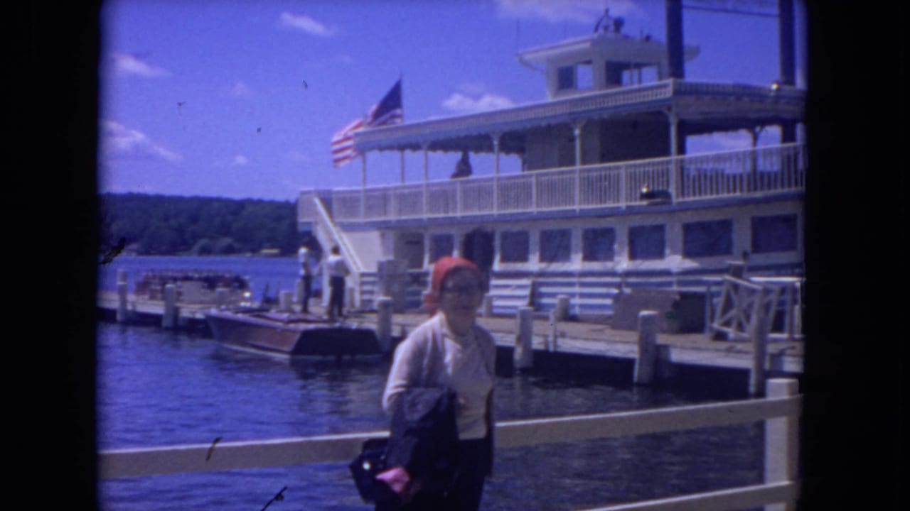 Woman stands near a dock railing with a white riverboat and American flag behind her.