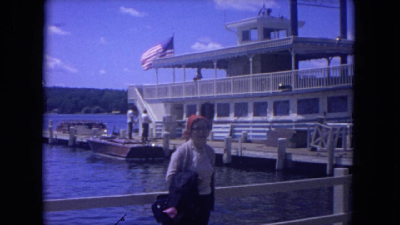 1972 riverfront footage shows a woman near the dock rail as passengers and a large white boat appear behind her.